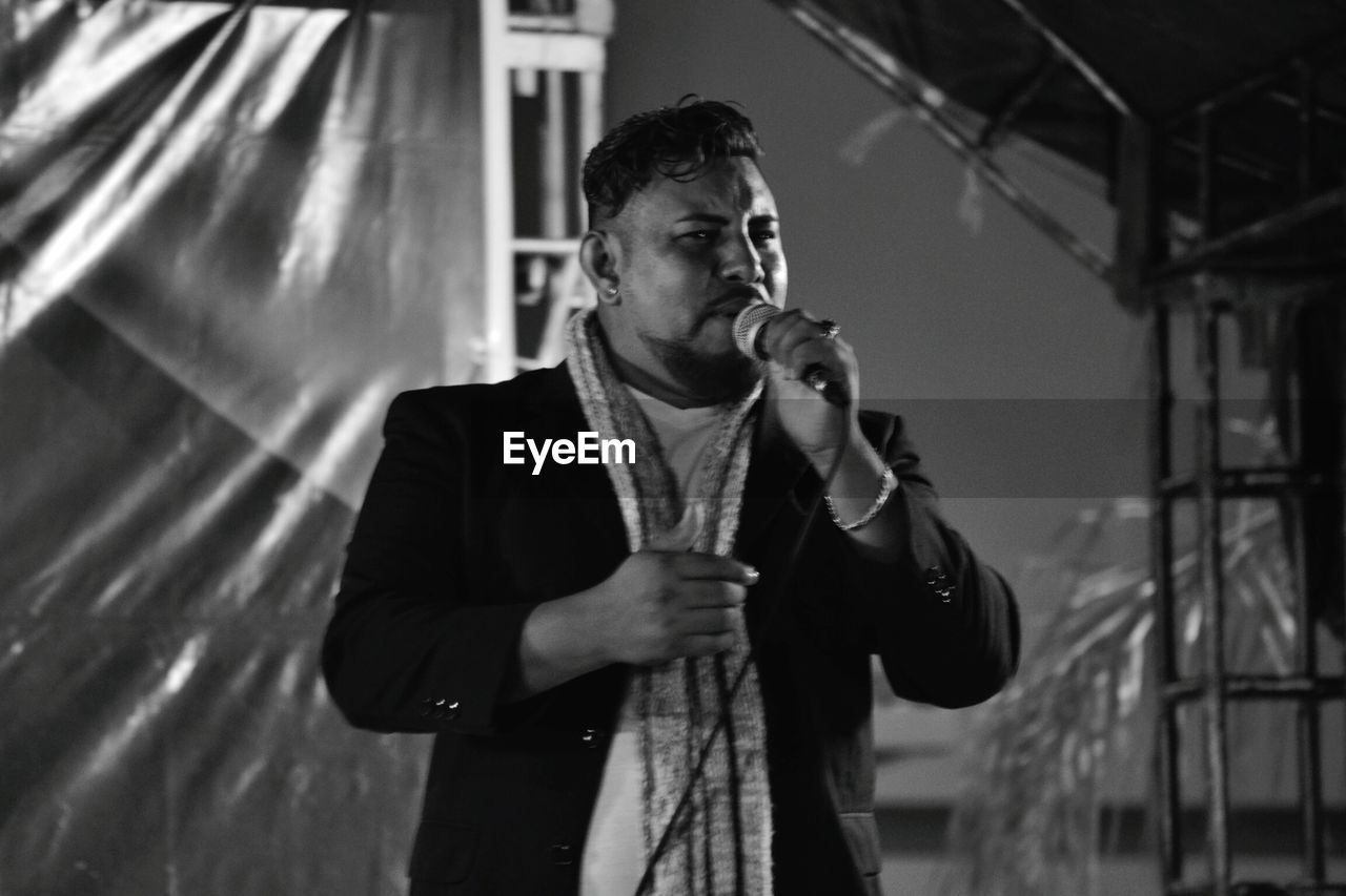 YOUNG MAN LOOKING AT CAMERA WHILE STANDING ON STAGE