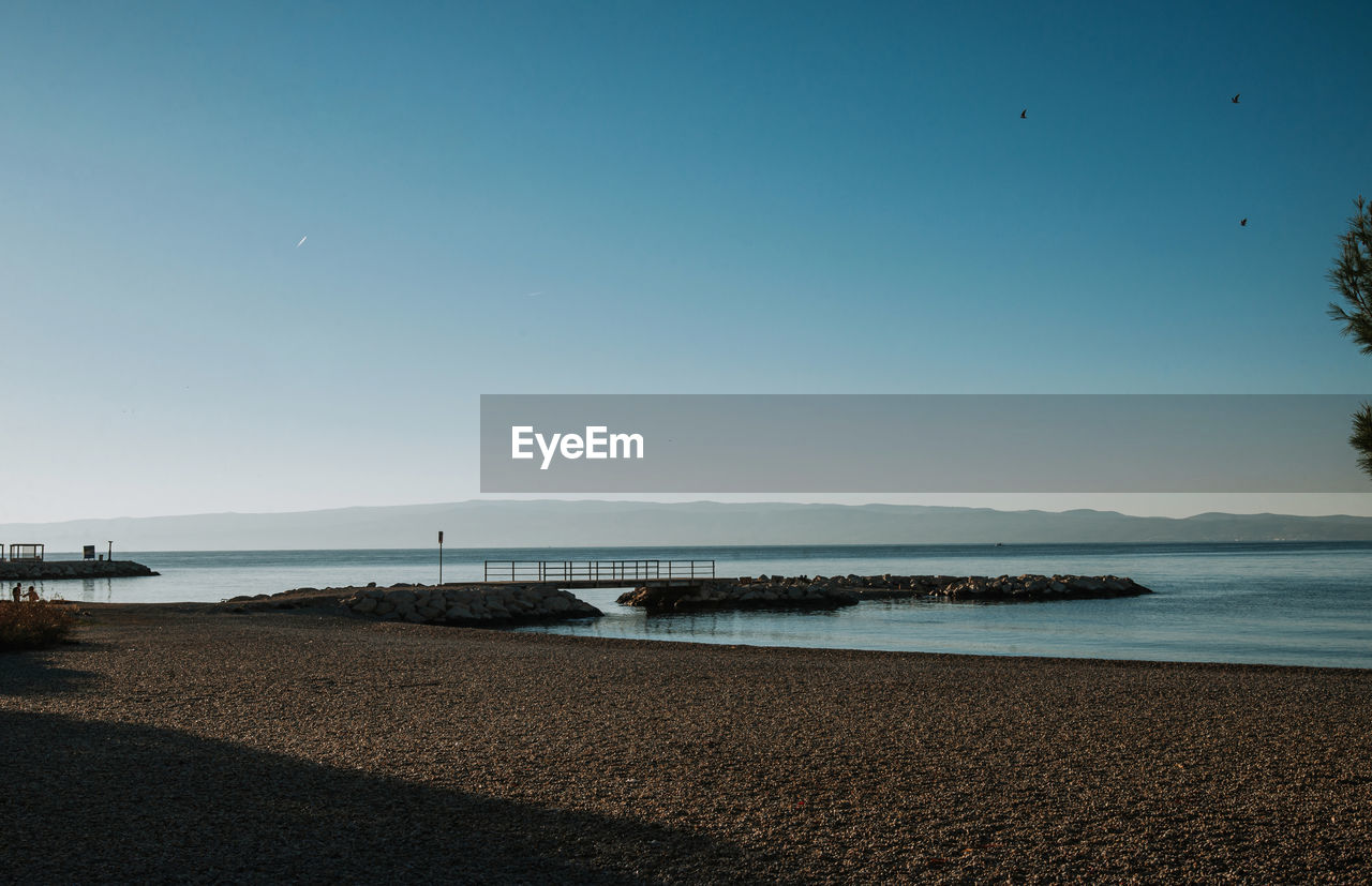water, sky, sea, horizon, beach, land, body of water, ocean, scenics - nature, nature, beauty in nature, shore, tranquility, dusk, clear sky, tranquil scene, coast, blue, wave, sand, travel destinations, morning, coastline, horizon over water, no people, bay, outdoors, travel, environment, idyllic, sunny, day, tree, holiday, landscape, seascape, water's edge, sunlight, reflection, tourism, copy space, trip, vacation, non-urban scene, animal wildlife, architecture, plant