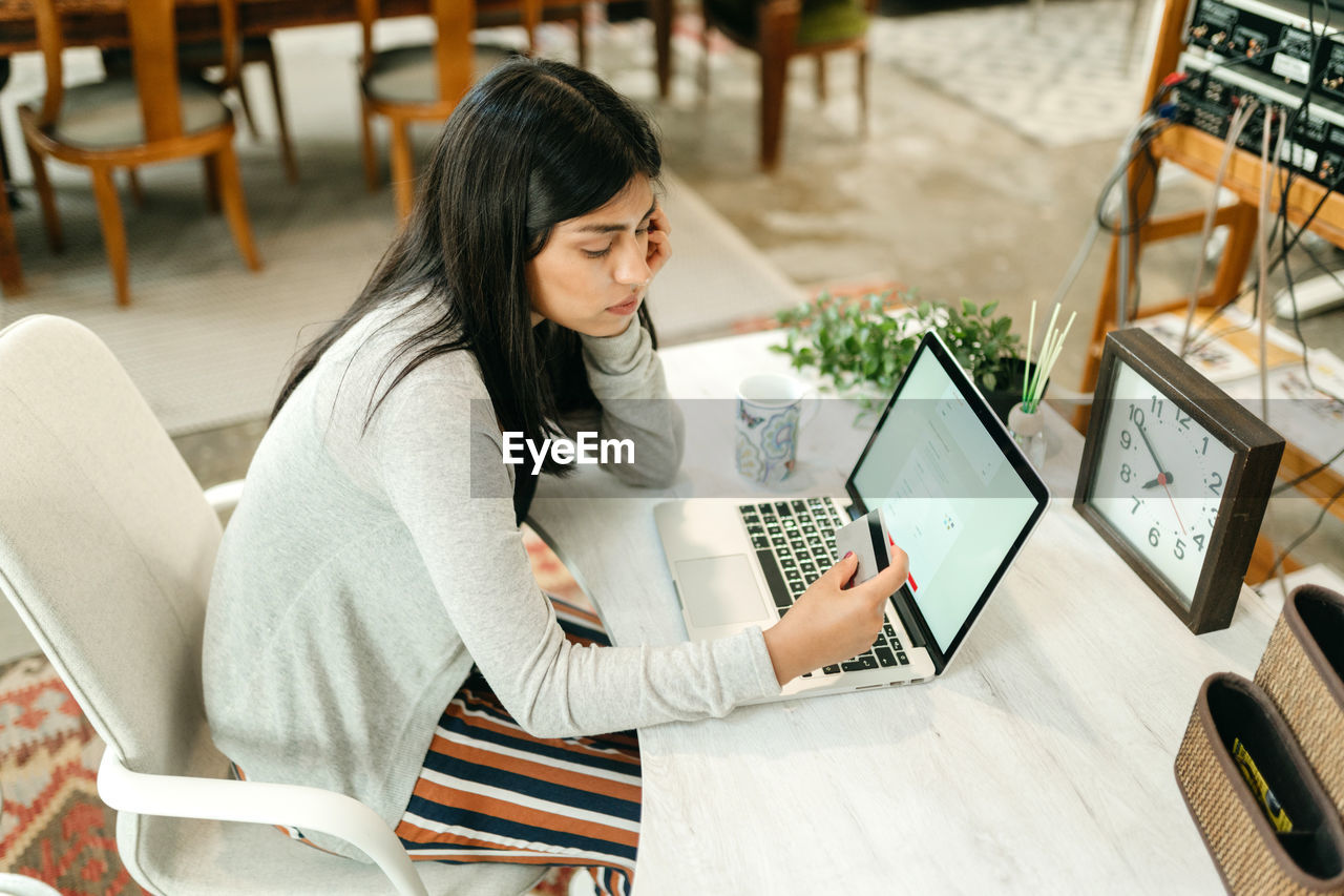 Side view female making purchase with plastic card for order during online shopping via laptop