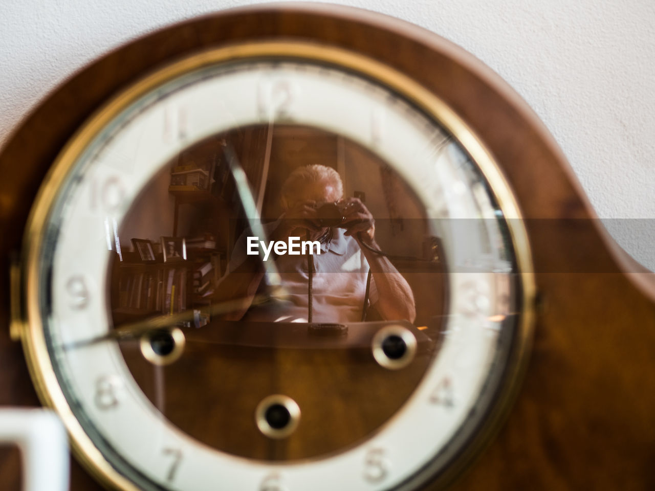 Senior man photographing with camera seen in clock at home