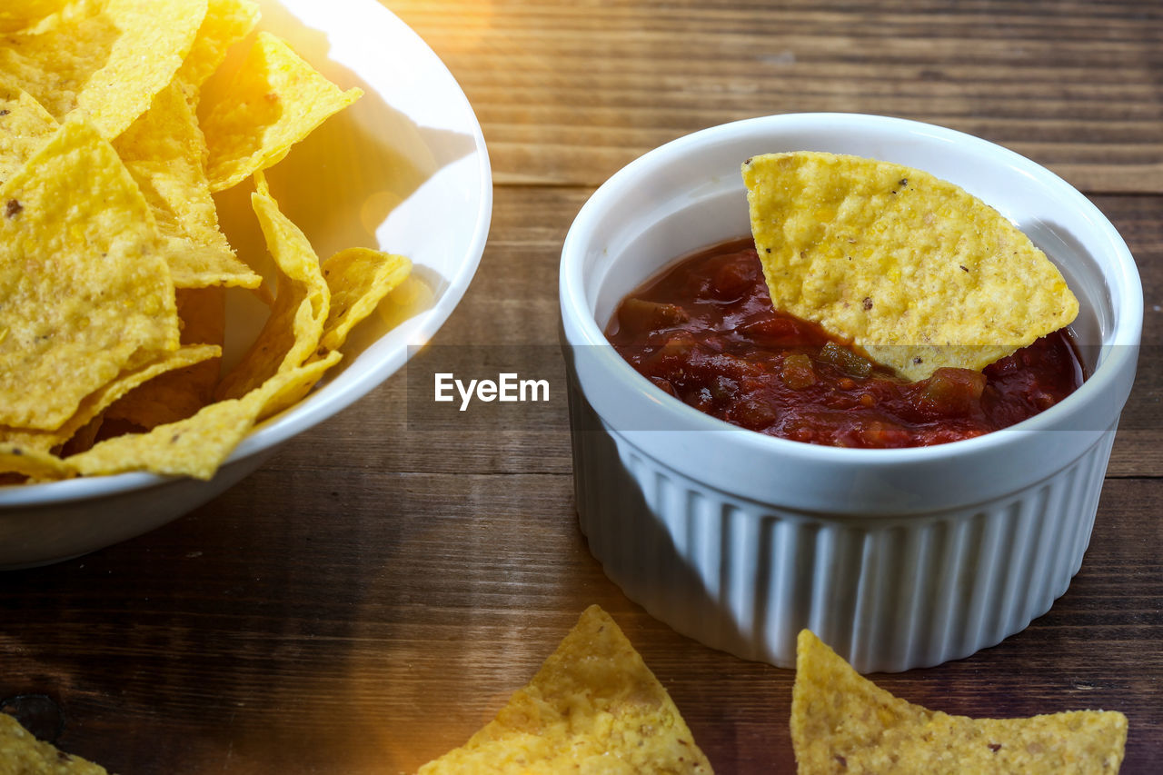 Tortilla chips inside bowl with salsa on wooden table with sun beam