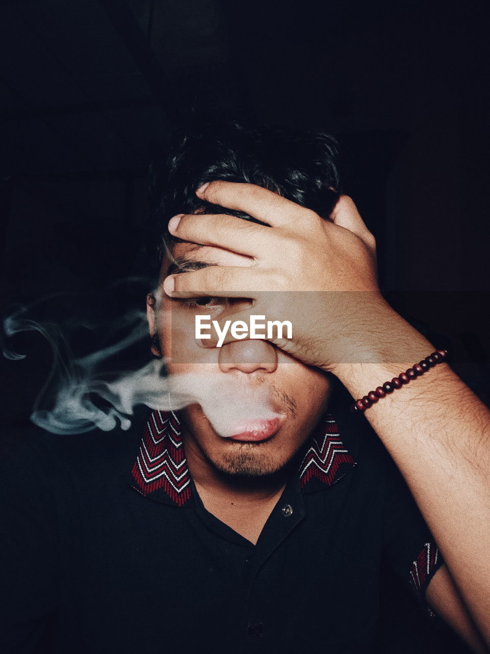 Close-up of young man smoking against black background