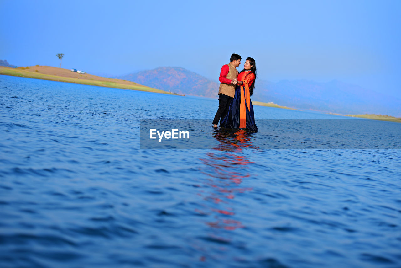 Tilt shot of couple standing on shallow water in lake against sky
