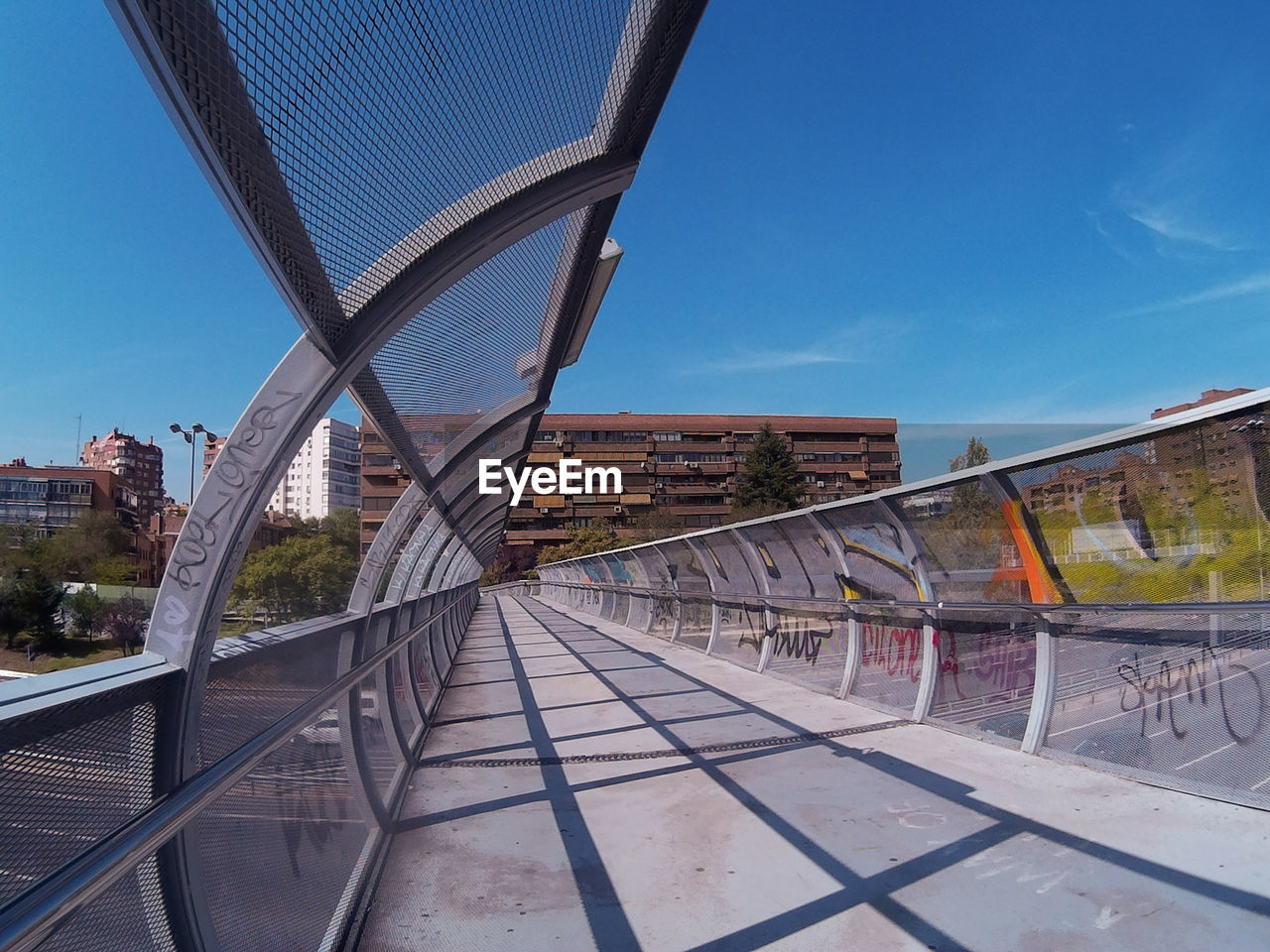 Futuristic bridge in madrid, spain, with a curved structure and a building at the back. blue sky