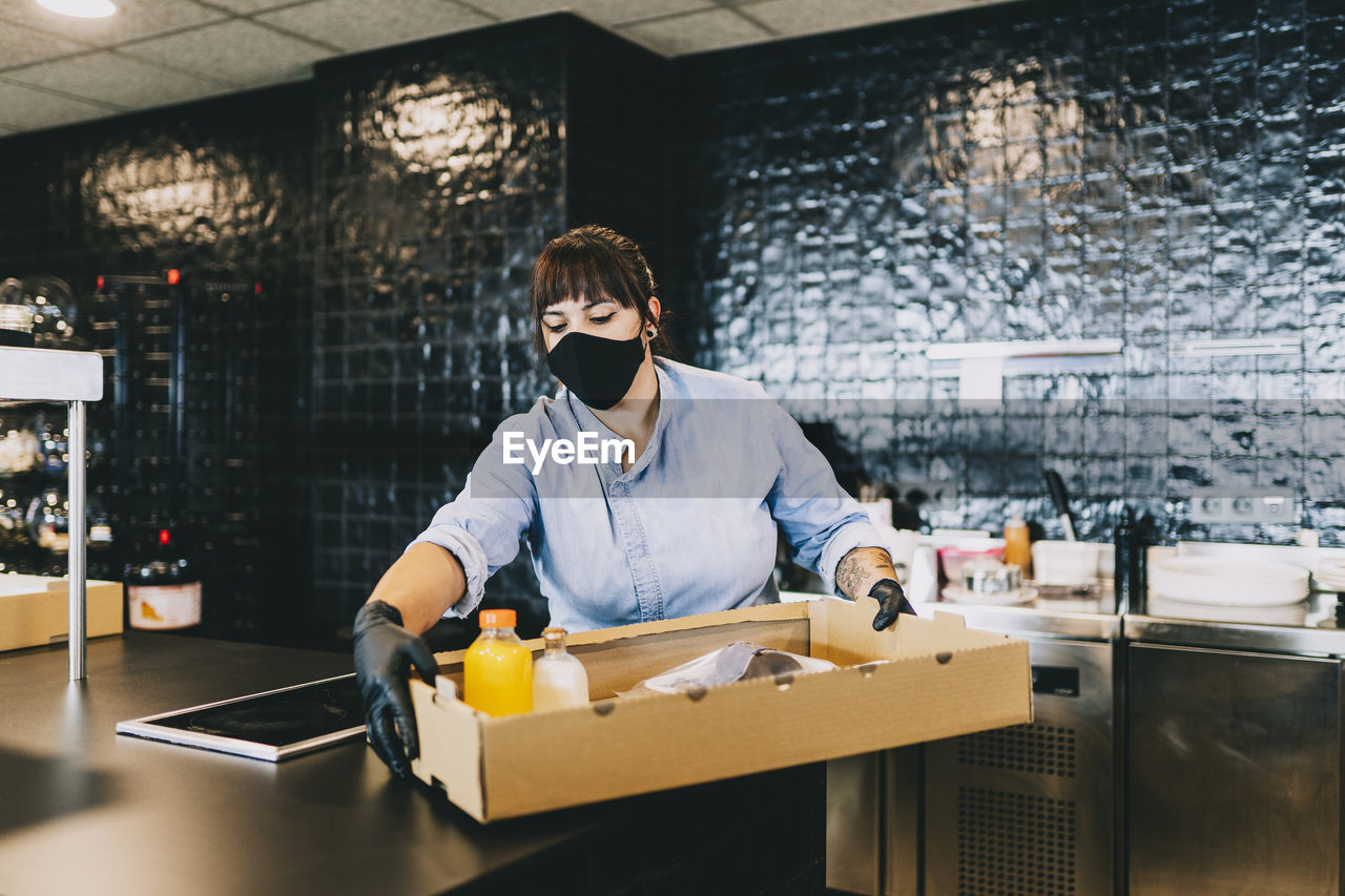 Female chef carrying cardboard box at counter in restaurant kitchen