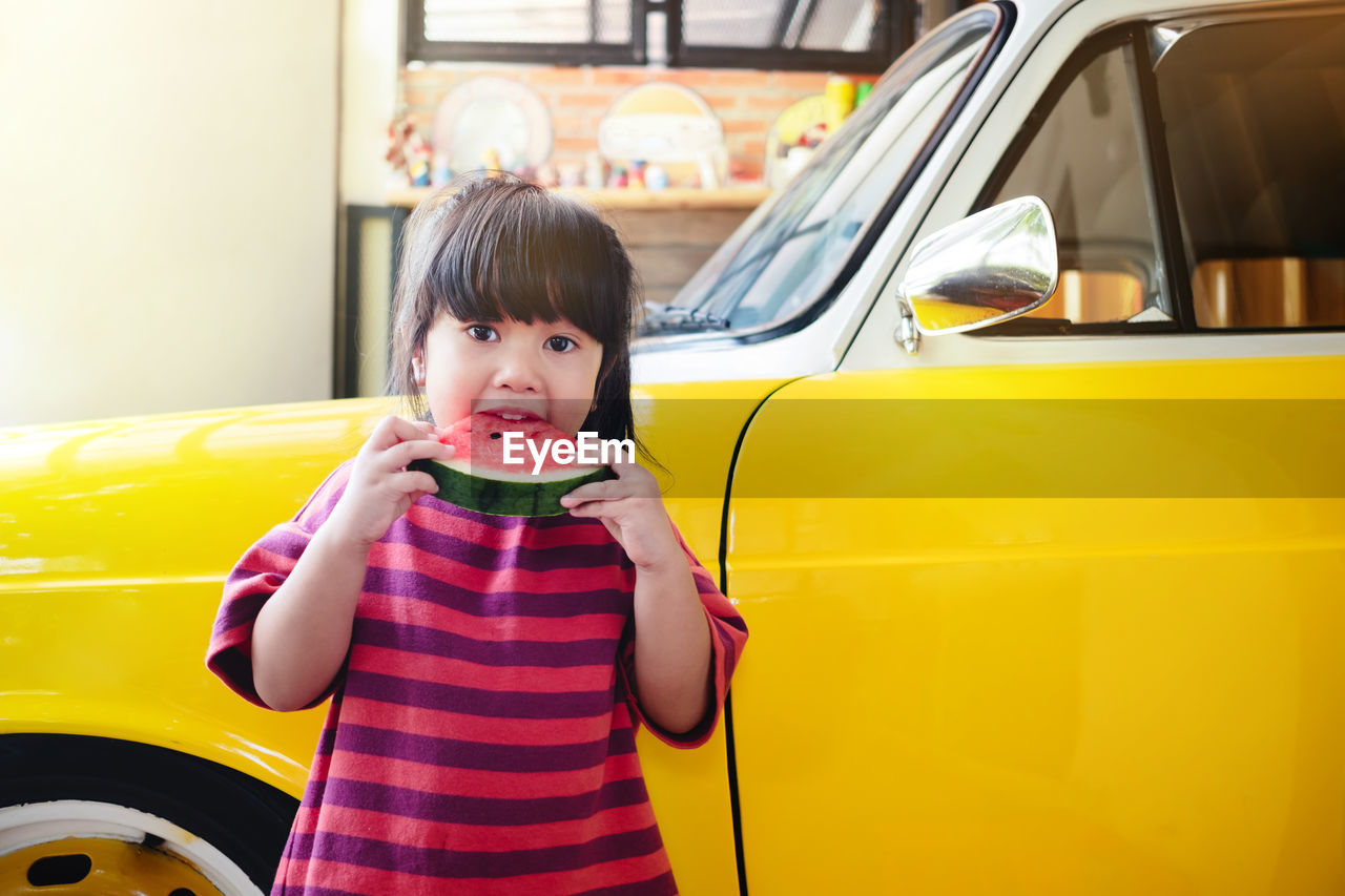 Portrait of girl eating watermelon by car