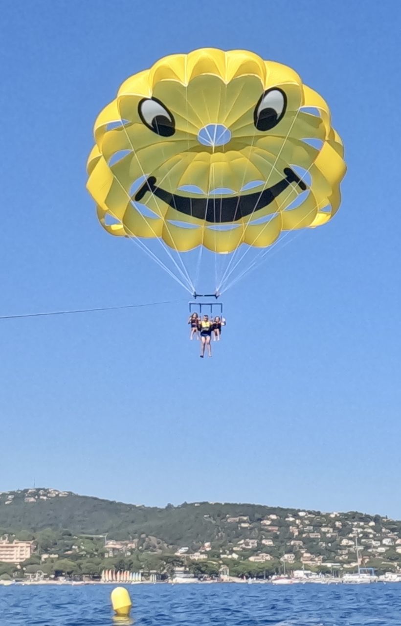 parasailing, sailing, sky, water, mid-air, adventure, nature, sea, sports, flying, parachute, extreme sports, clear sky, transportation, water sports, blue, toy, windsports, day, leisure activity, paragliding, motion, fun, yellow, holiday, vacation, sunny, kite sports, outdoors, trip, joy, air vehicle, multi colored, recreation, travel, balloon, mode of transportation