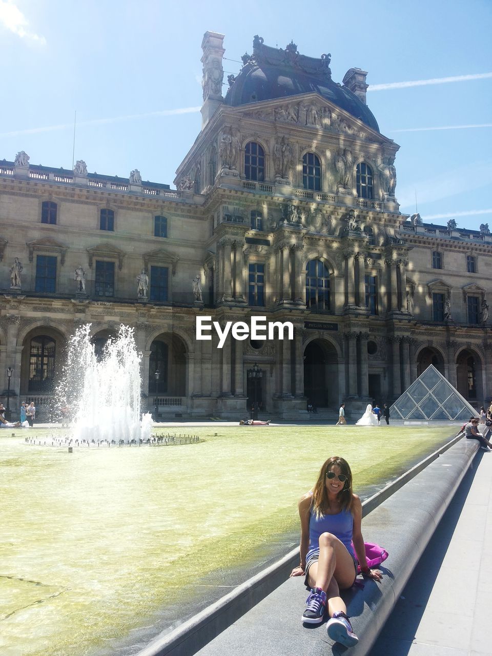 Full length of woman sitting at town square during sunny day