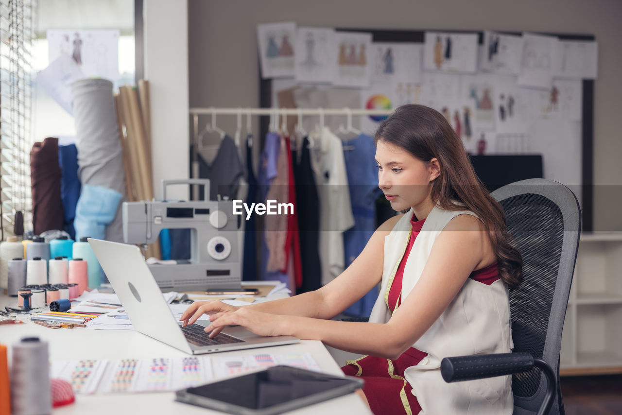 A lovely asian woman fashion designer sits at her workstation in her studios 