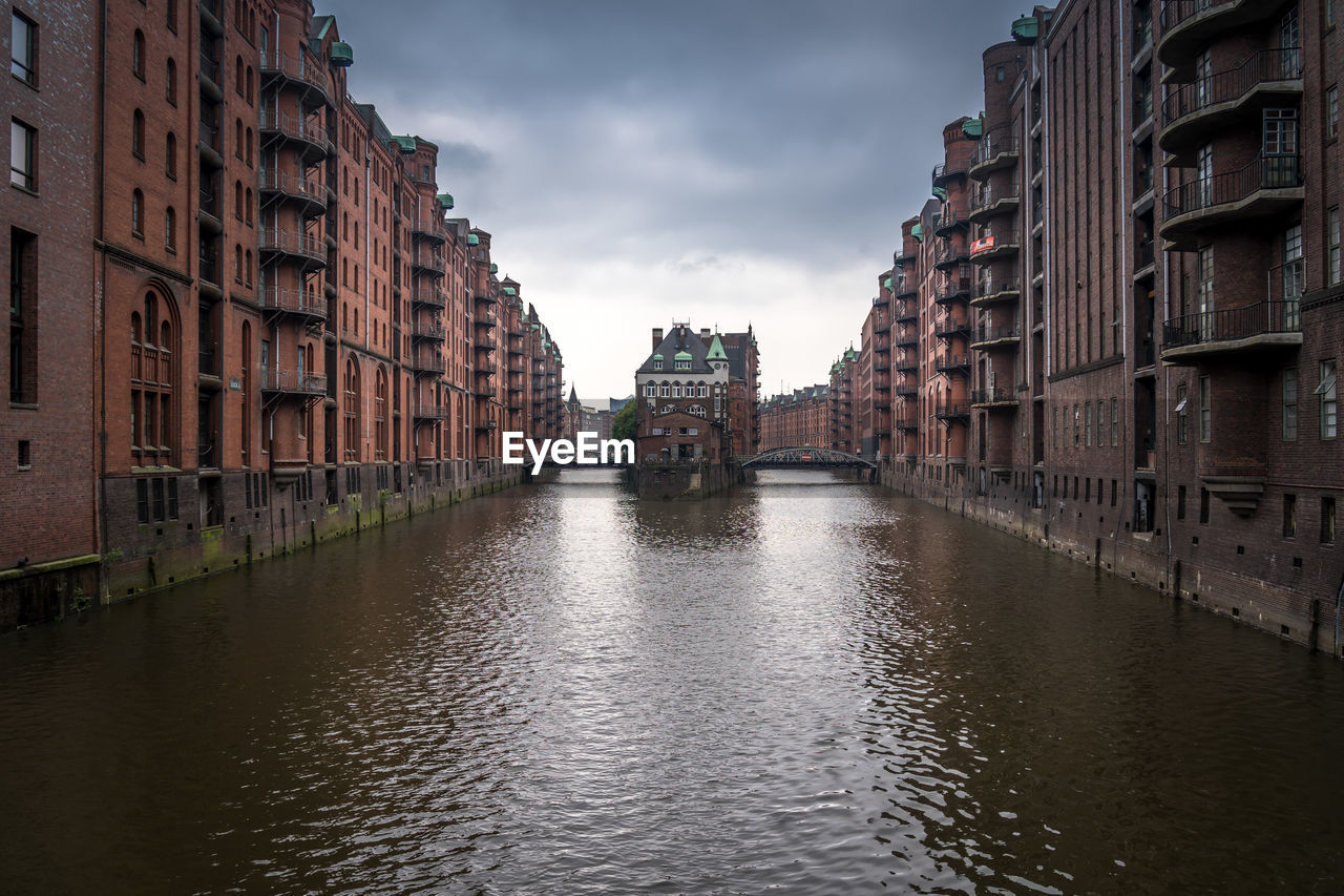 Canal amidst buildings in city against sky