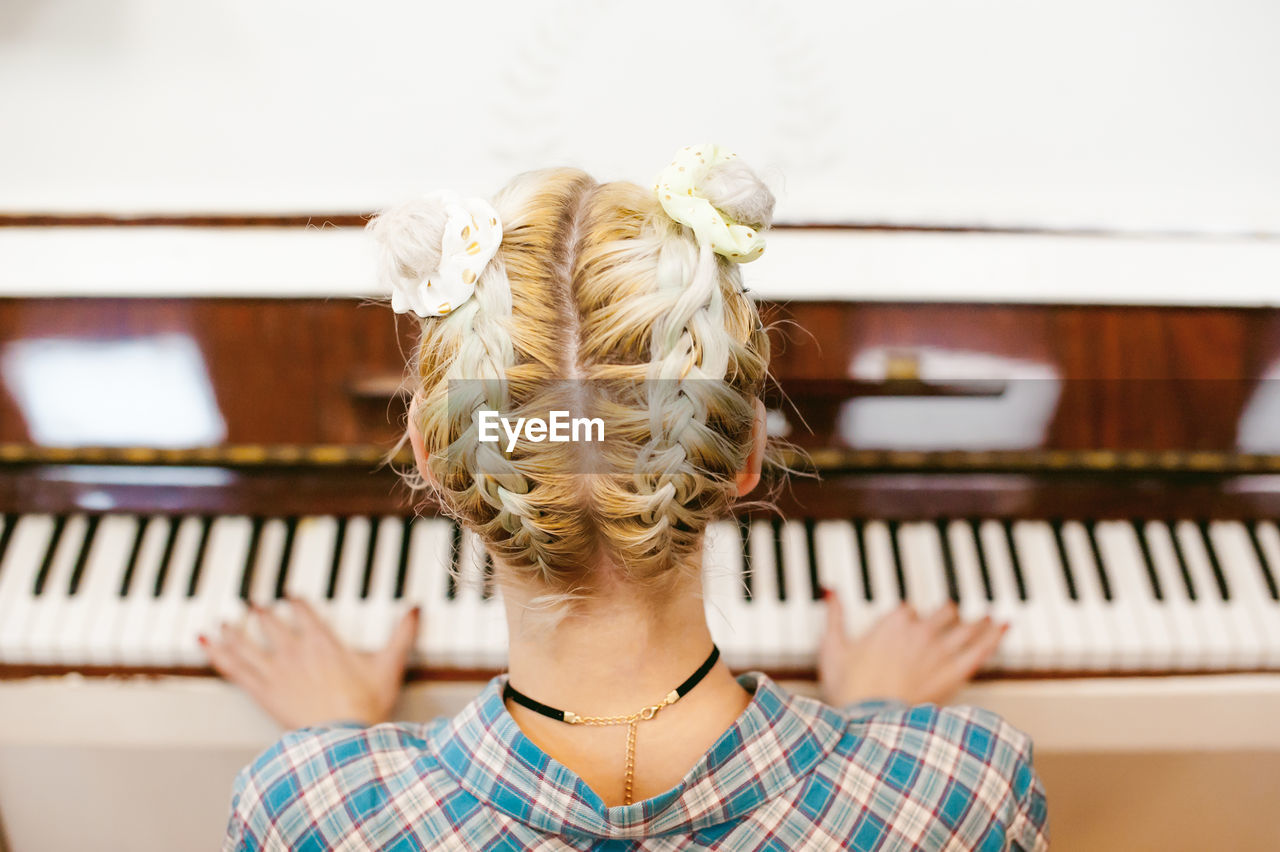 Rear view of woman playing piano at home