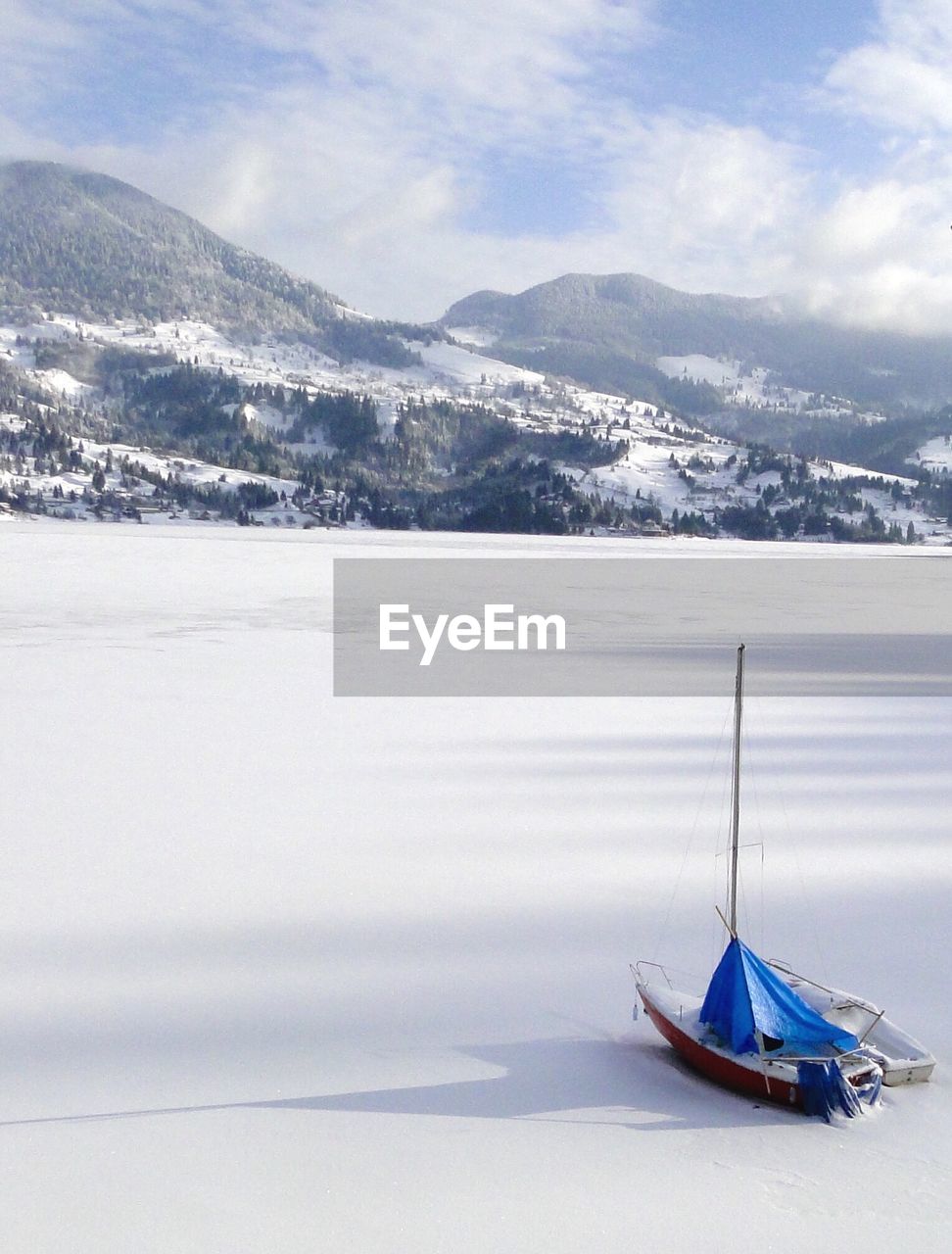 High angle view of boat on snow covered landscape by mountains against sky