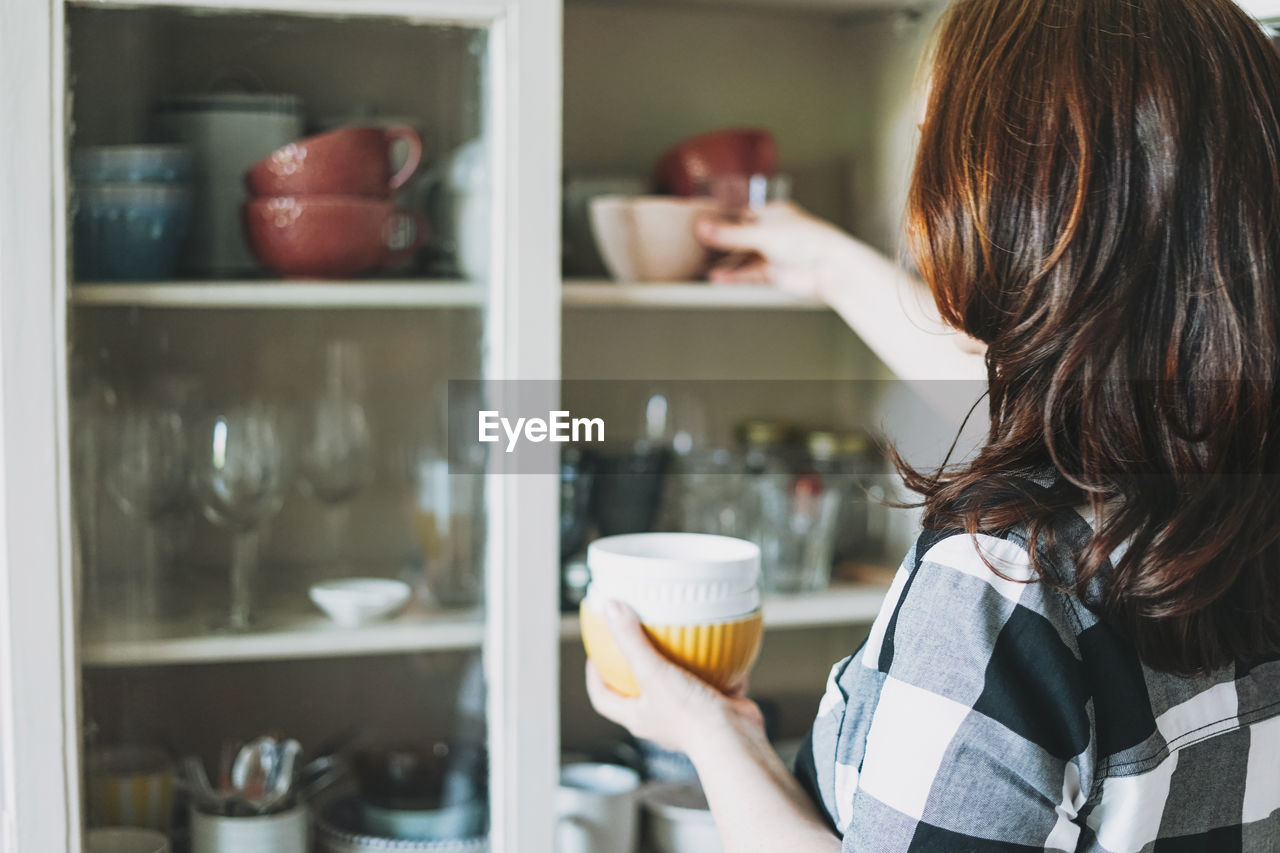 Side view of mature woman arranging bowls on shelf at home