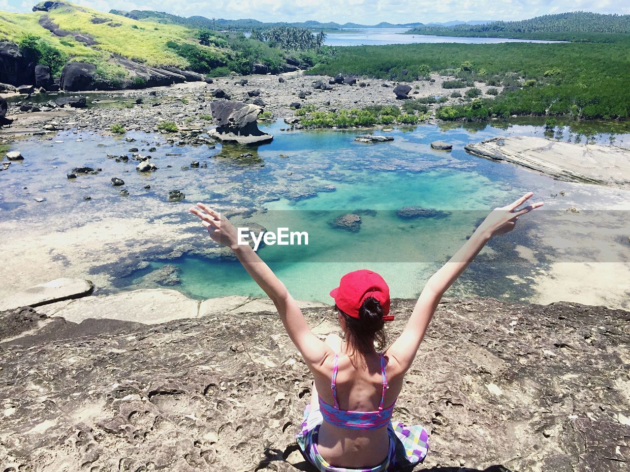 Rear view of woman with arms raised by lake on sunny day