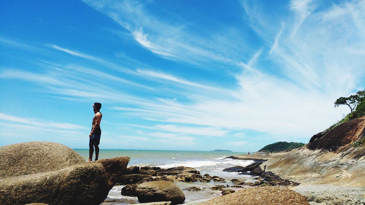 REAR VIEW OF MAN PHOTOGRAPHING ON SEA SHORE AGAINST SKY