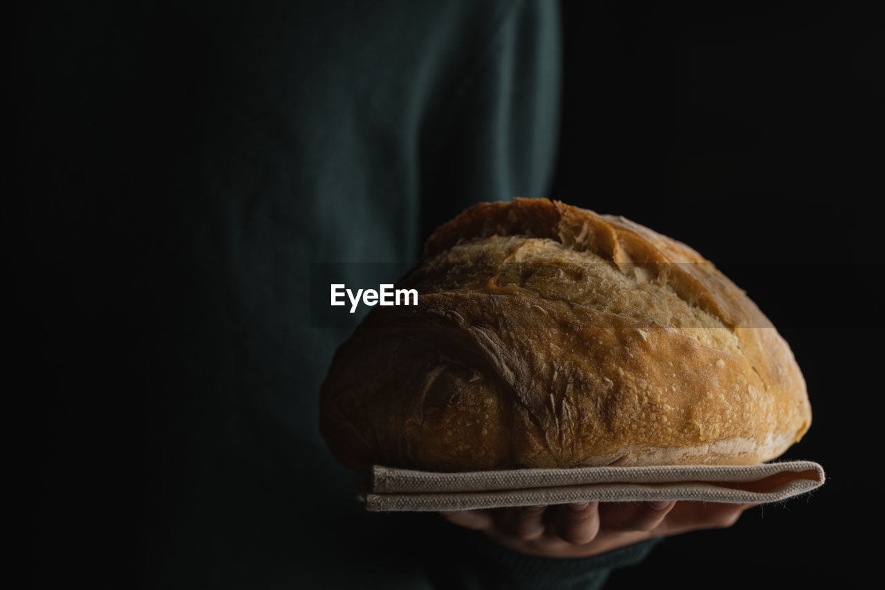 Close-up of hand holding homemade bread over black background