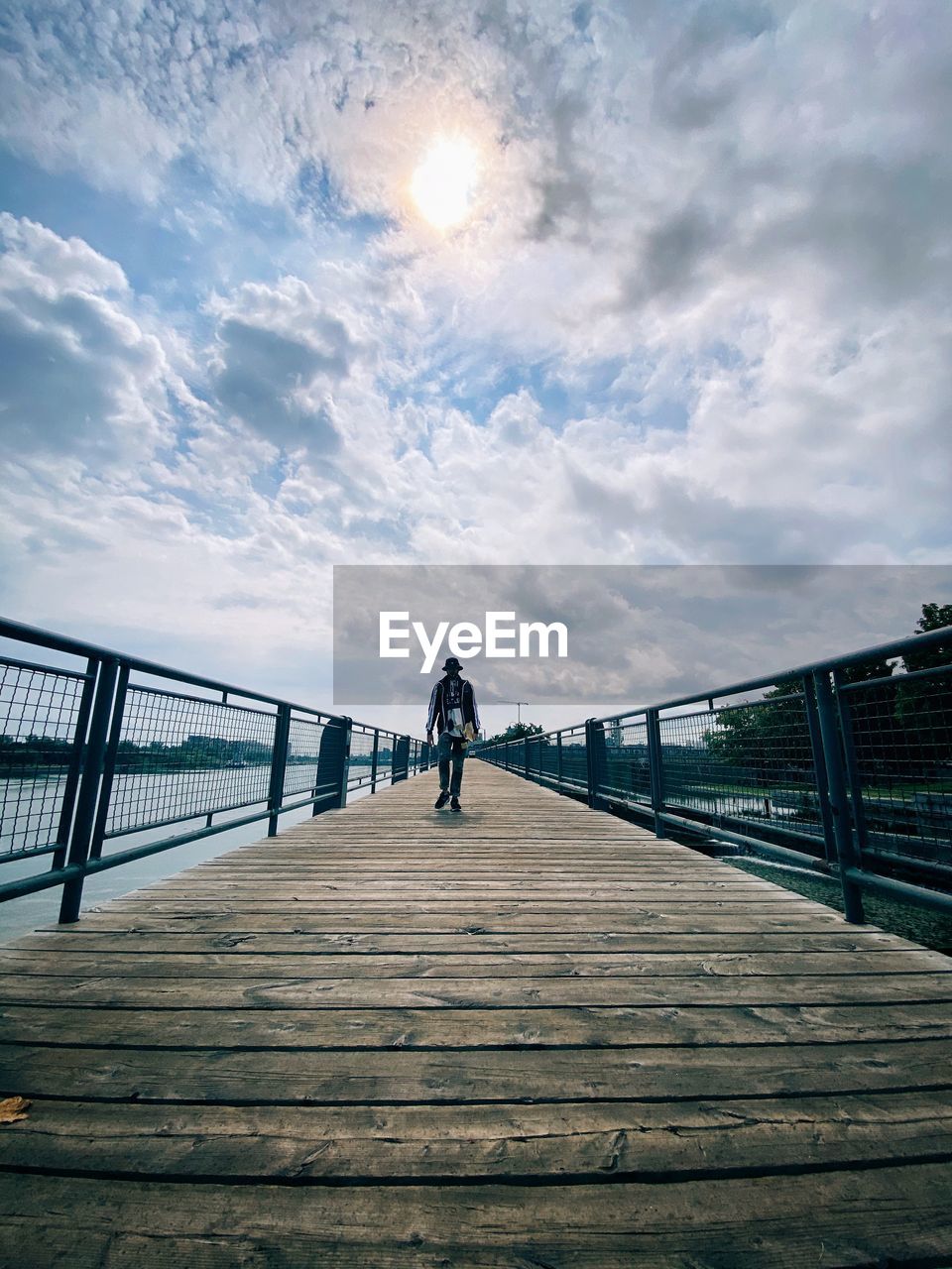 Skateboarder in front of cloudy sky standing on footbridge