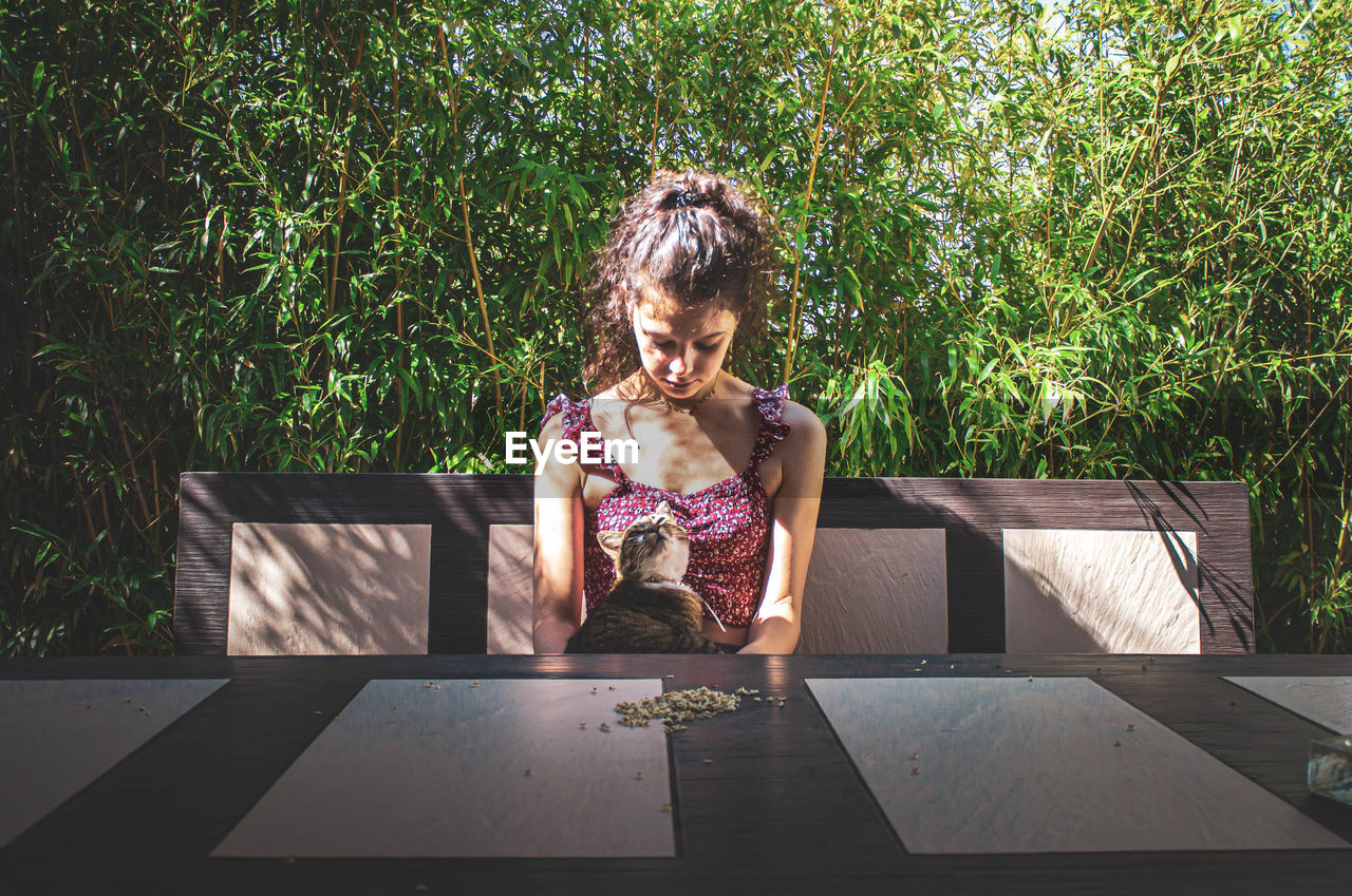 Young girl with her cat sitting at the table against bamboo leaves