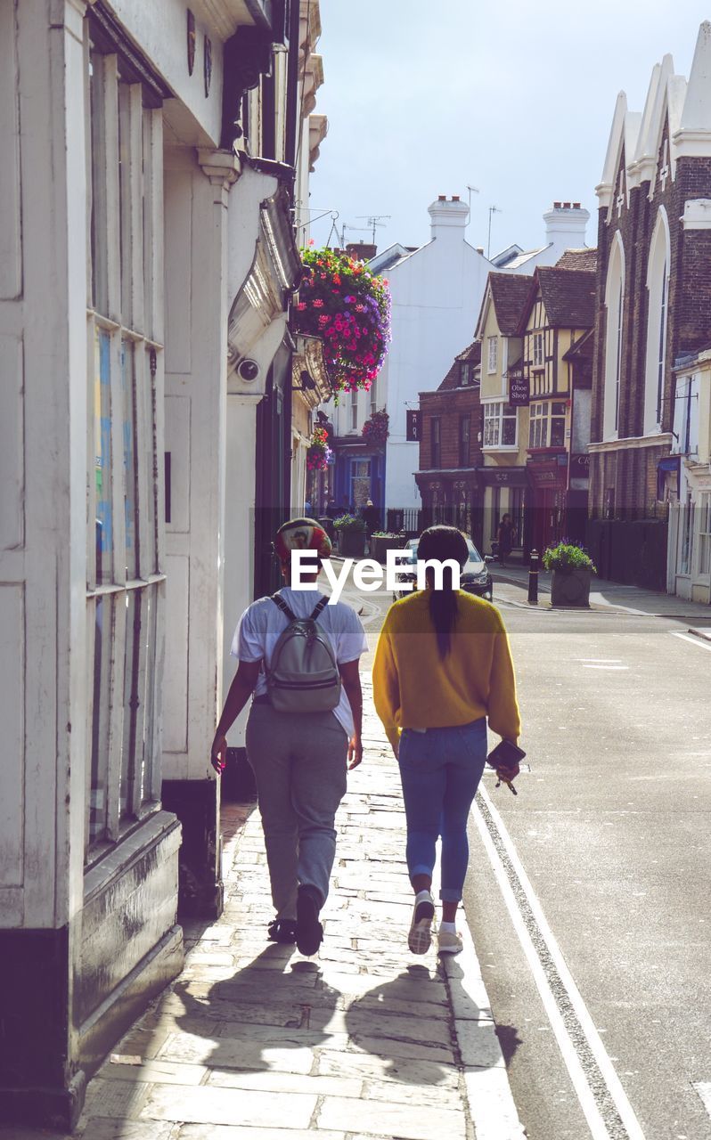 Rear view of  women walking on street amidst buildings