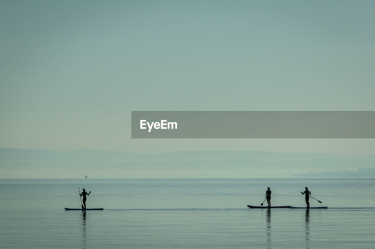 Silhouette people on boat in lake against sky