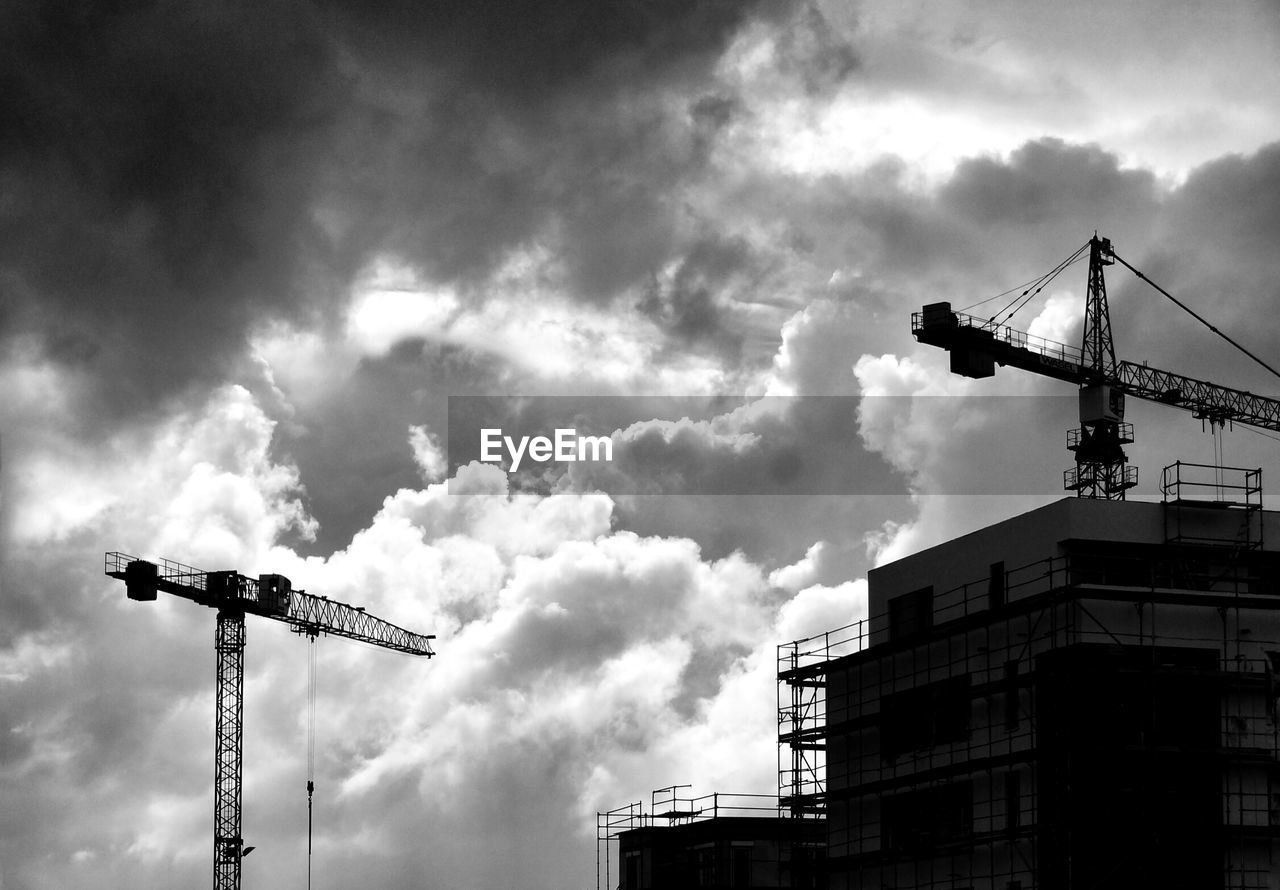 High section of cranes against cloudy sky