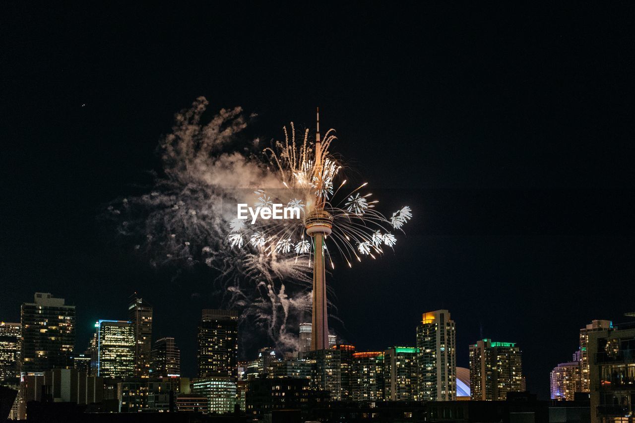 Low angle view of firework display by cn tower against sky at night