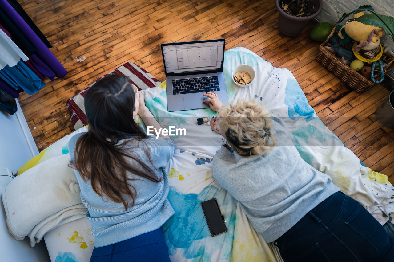 High angle view of female friends using laptop while resting on bed in bedroom at home