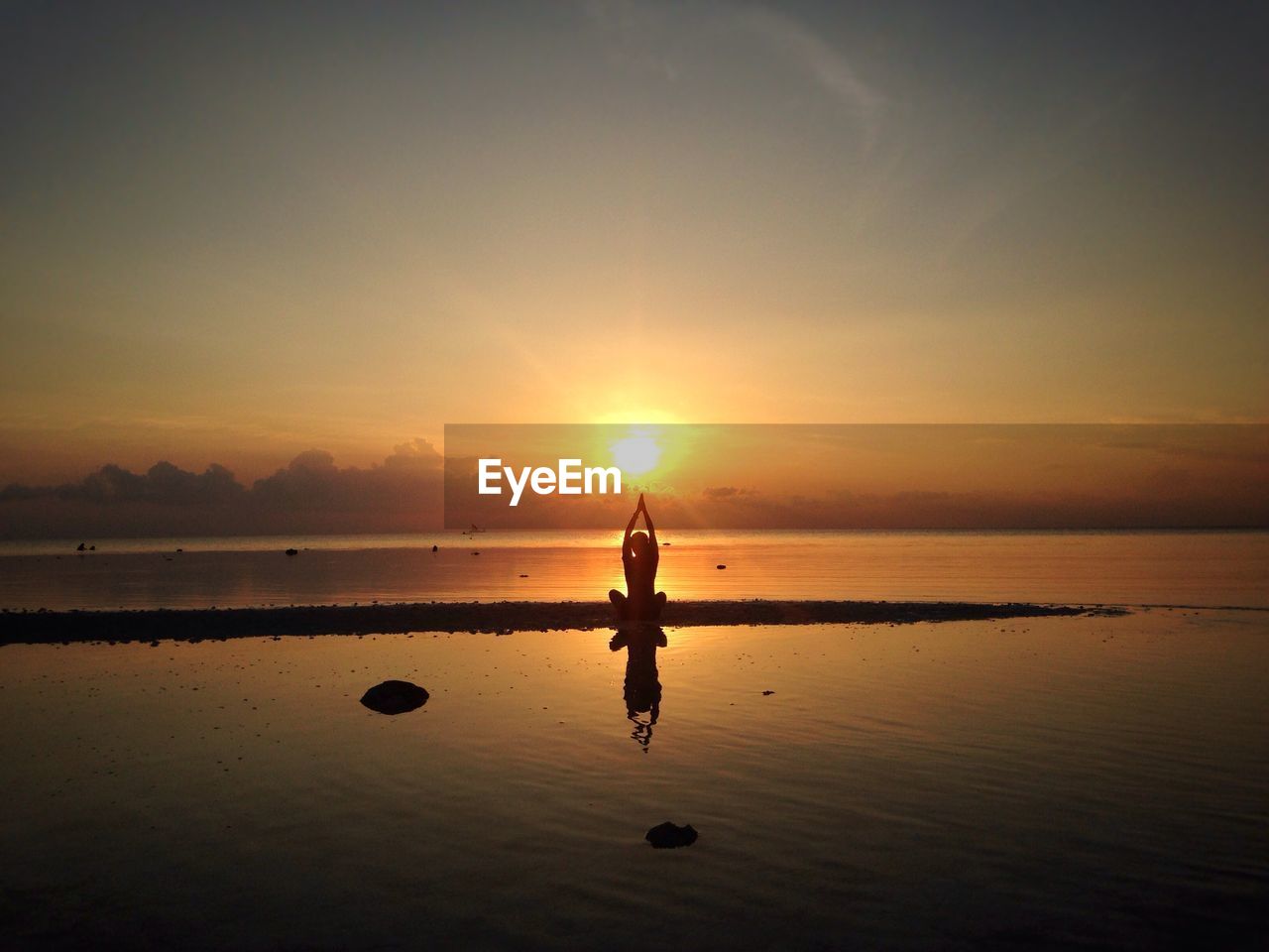 Silhouette person doing yoga at beach against sky during sunset