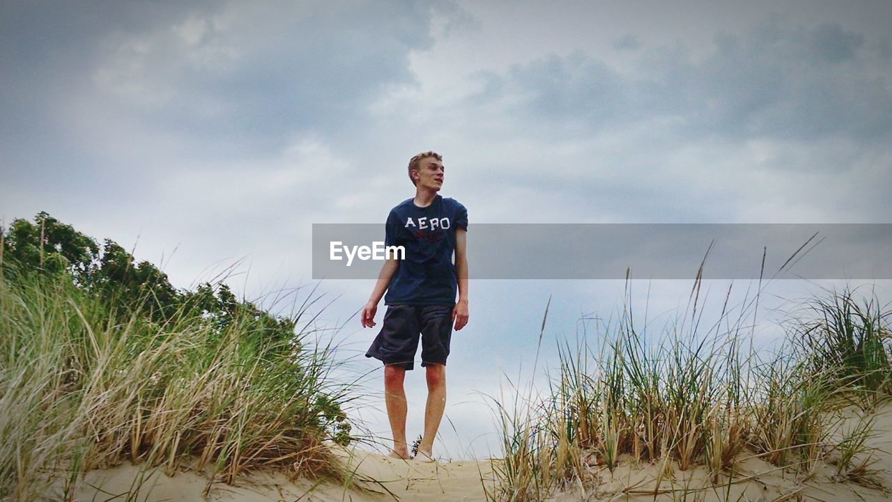 Low angle view of man standing on sandy field against cloudy sky