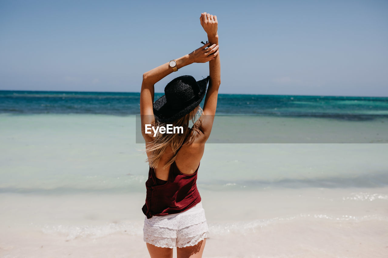 Woman in hat standing at beach against clear sky in sunny day