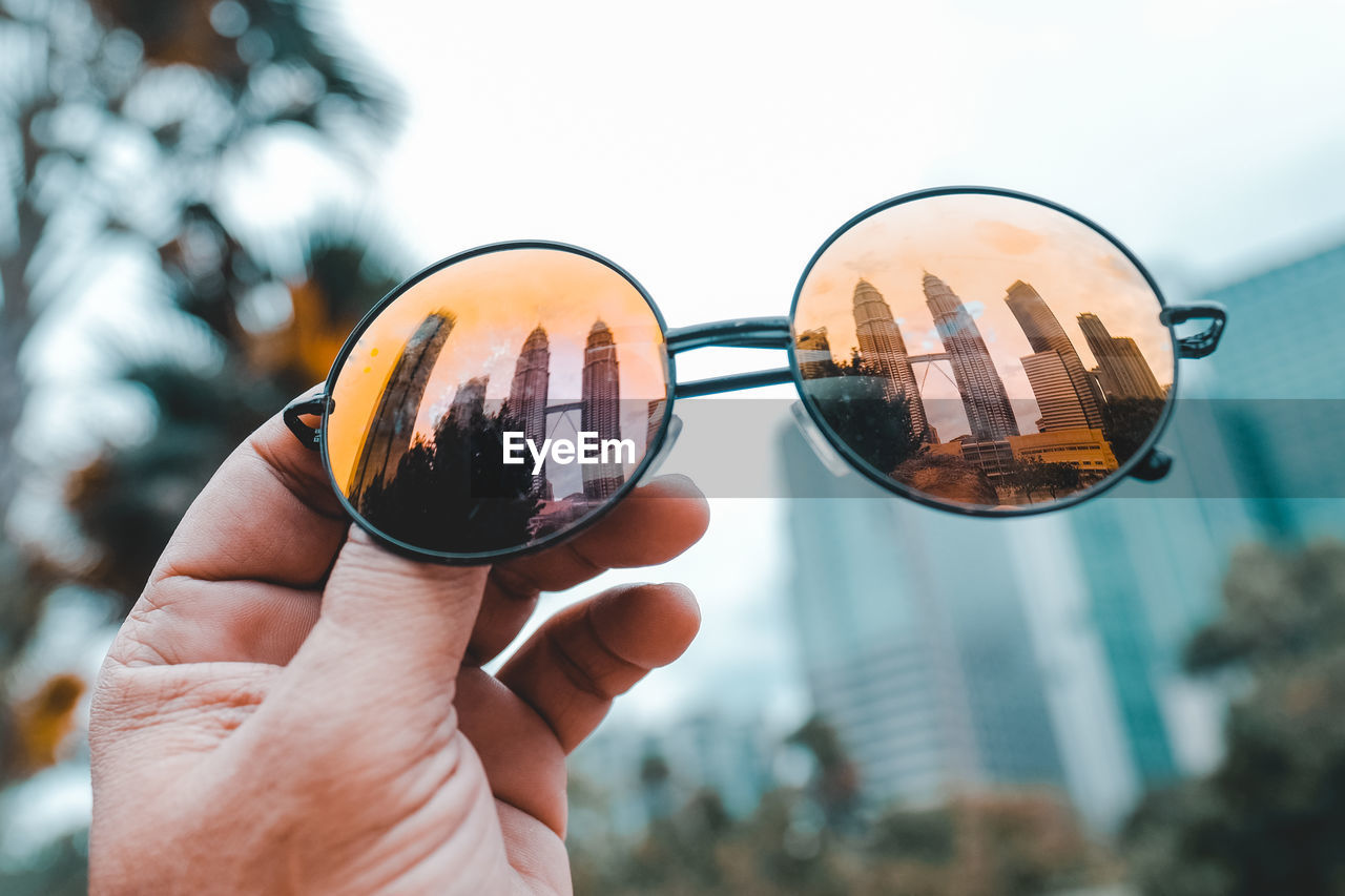 Cropped hand holding sunglasses with reflection of petronas towers