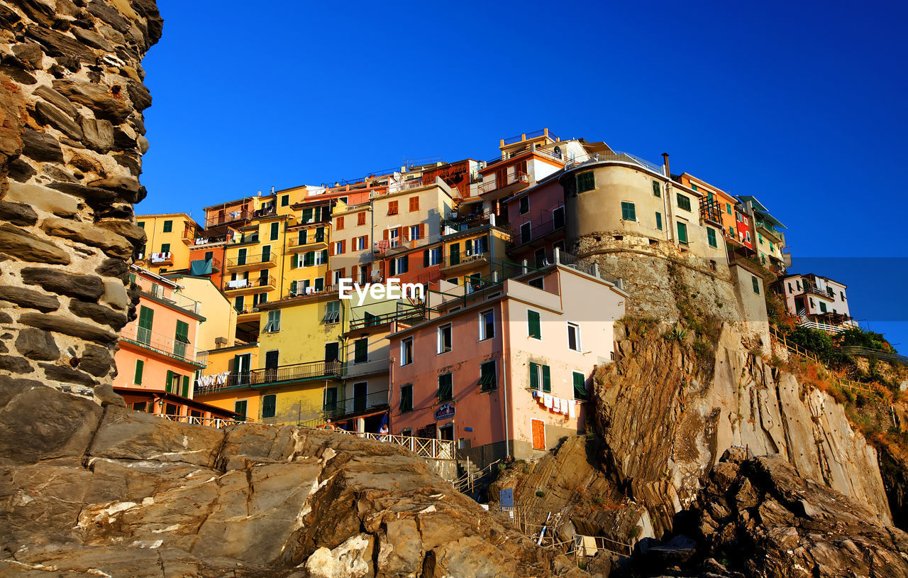 Low angle view of residential buildings on rocky mountain against clear blue sky