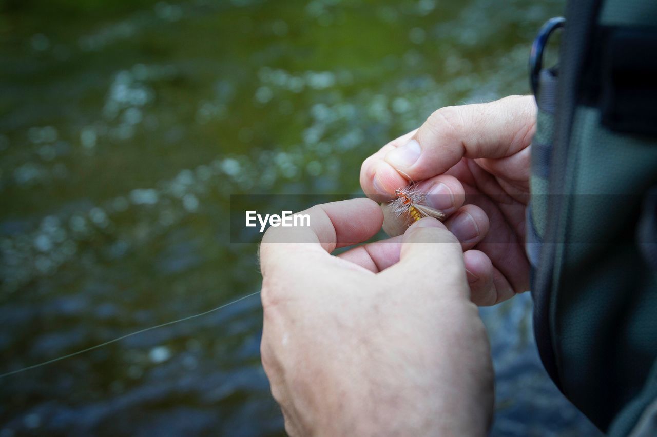 Cropped hand holding fishing tackle over river