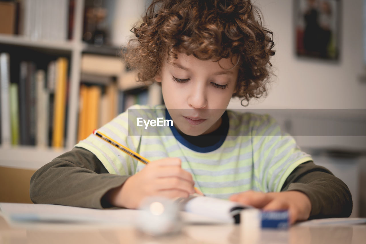 Cute boy writing in book on table at home