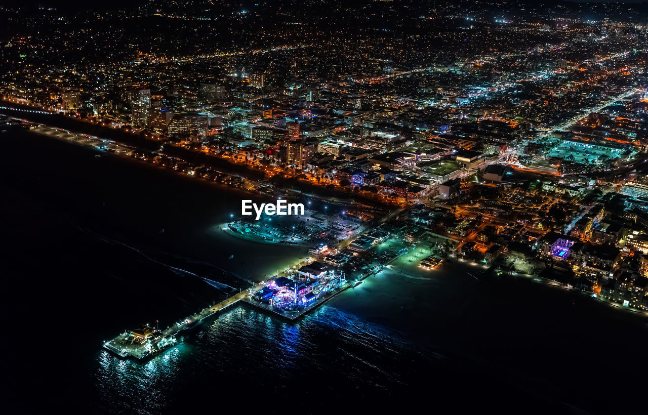Aerial view of sea by illuminated cityscape at night