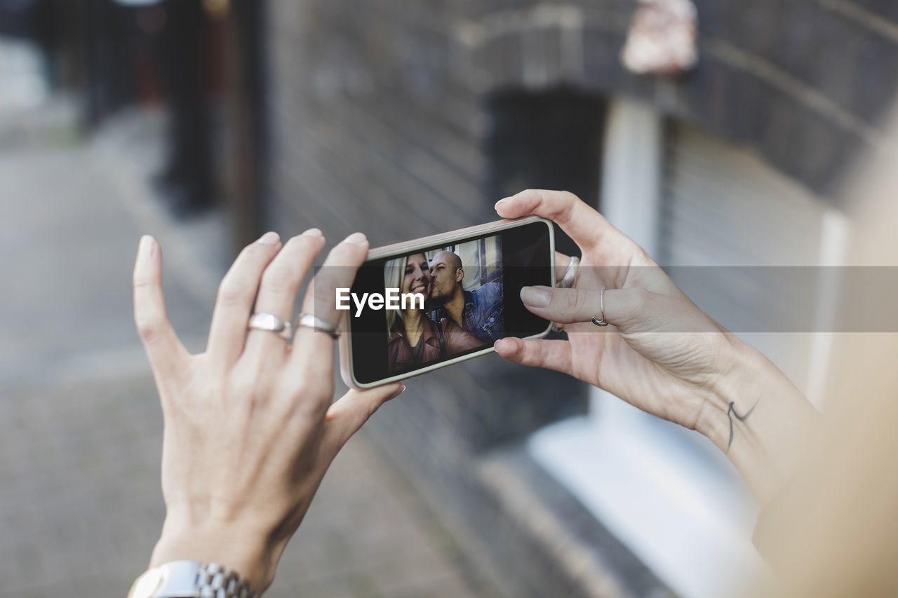 Man kissing woman as she takes selfie through smart phone