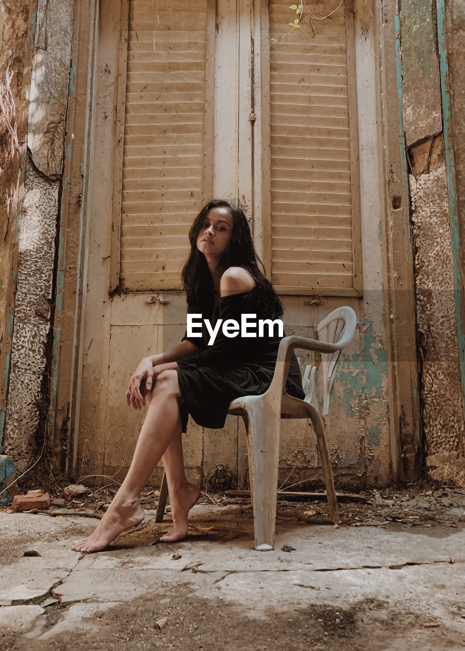 Portrait of young woman sitting on old abandoned house