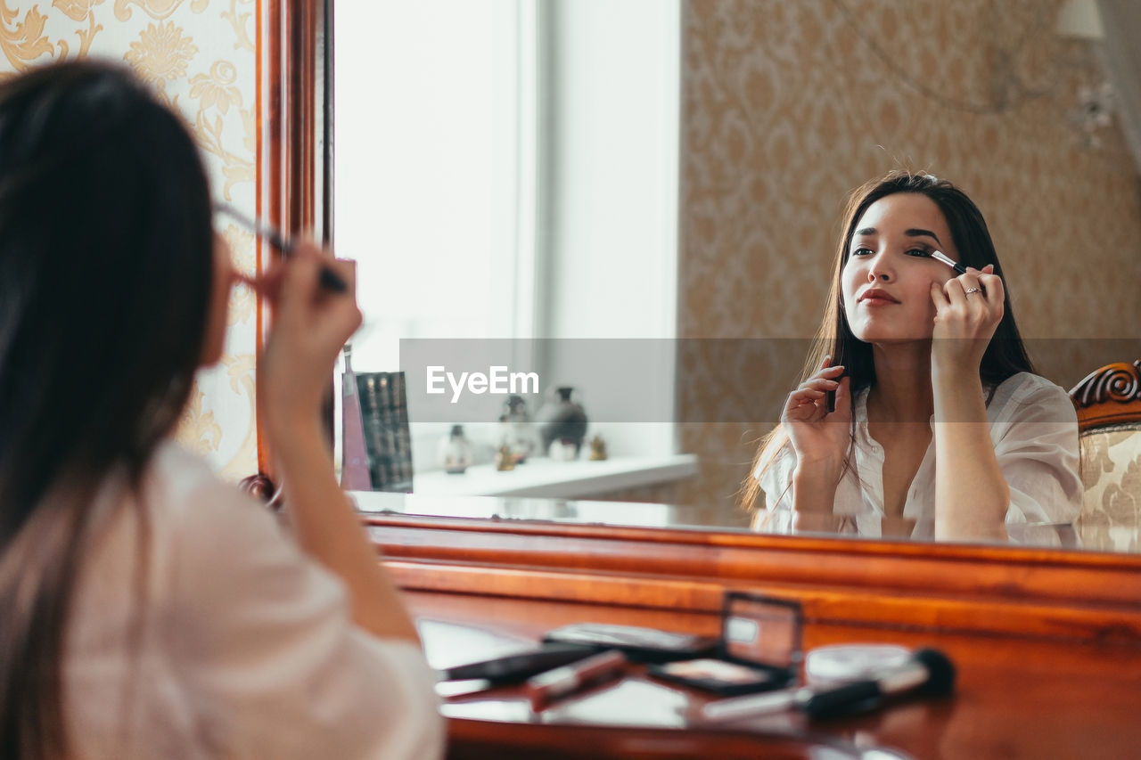 Young woman doing make-up while looking at mirror