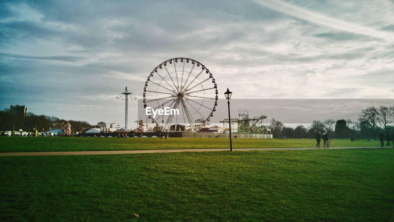 Ferris wheel at park against cloudy sky