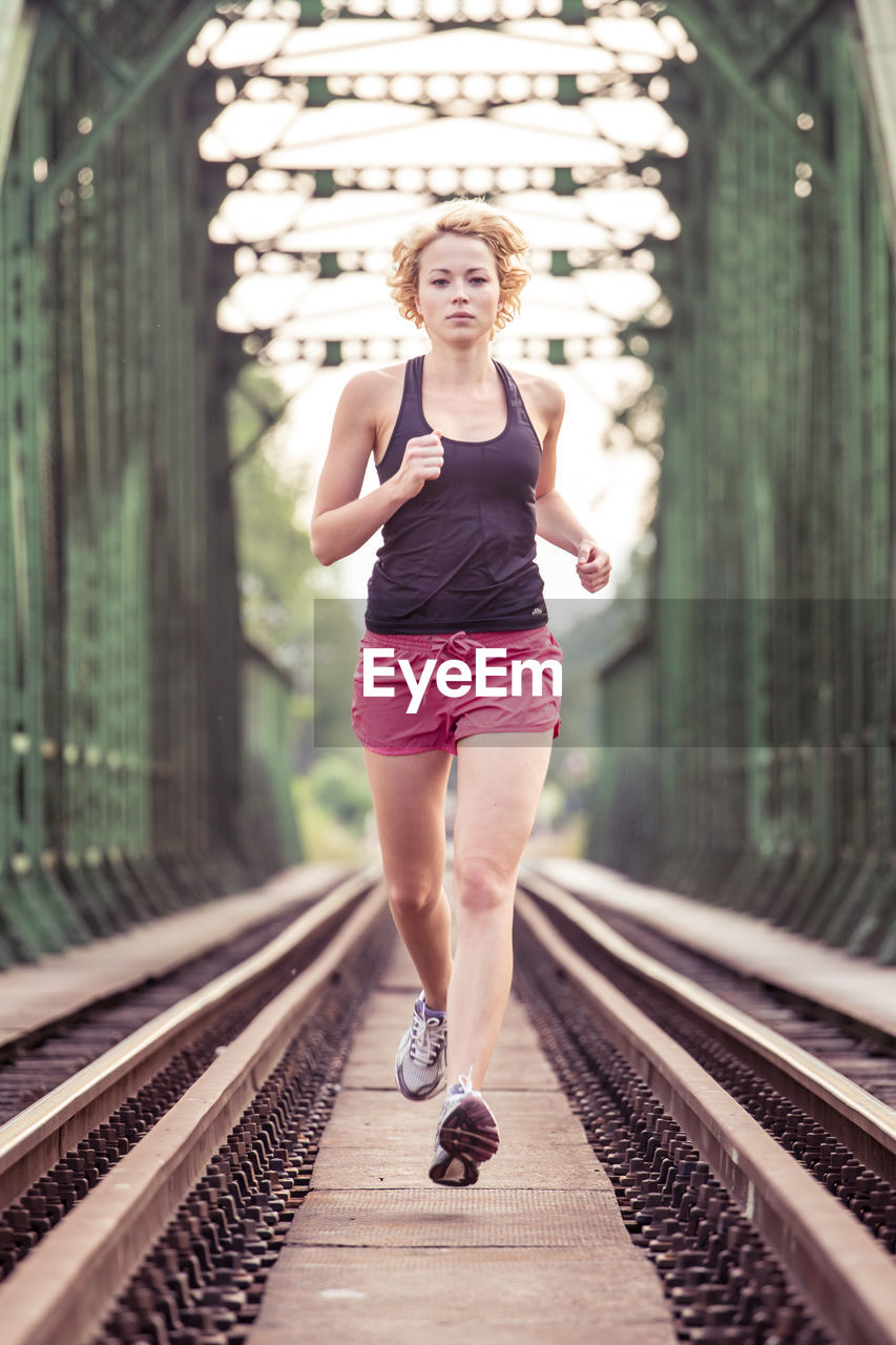 Full length portrait of woman running on railroad tracks