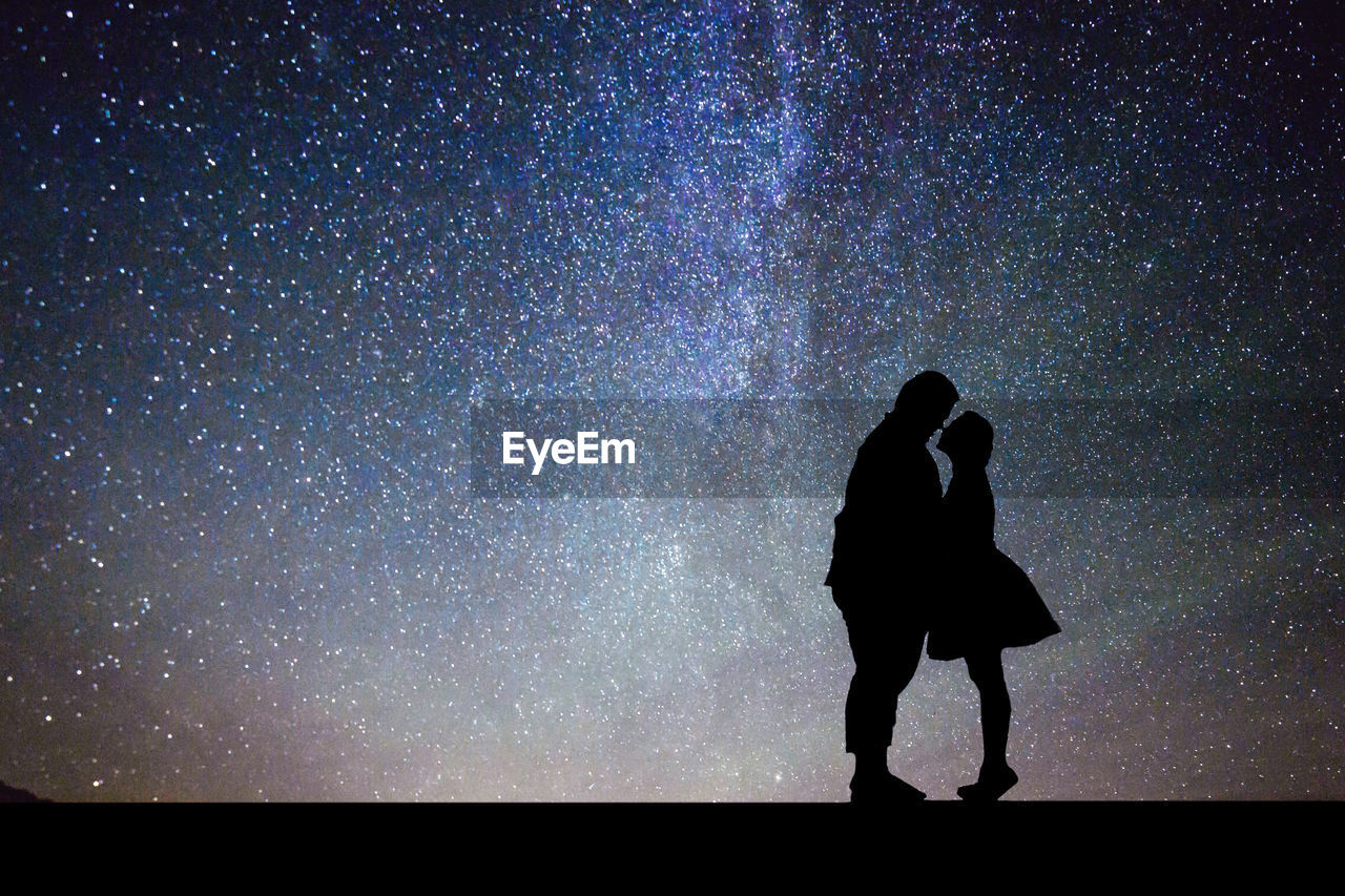 Side view of silhouette couple romancing while standing against star field at night