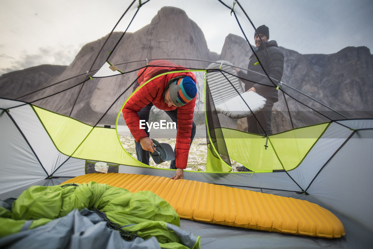 Two men set up sleeping pads in their tent during climbing trip.