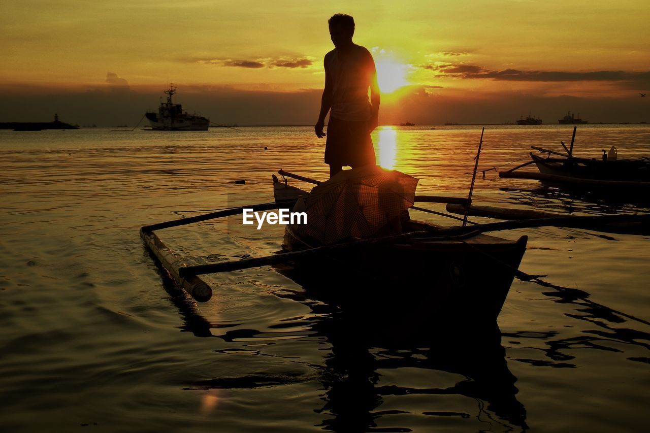 SILHOUETTE MAN FISHING ON BOAT AT SUNSET