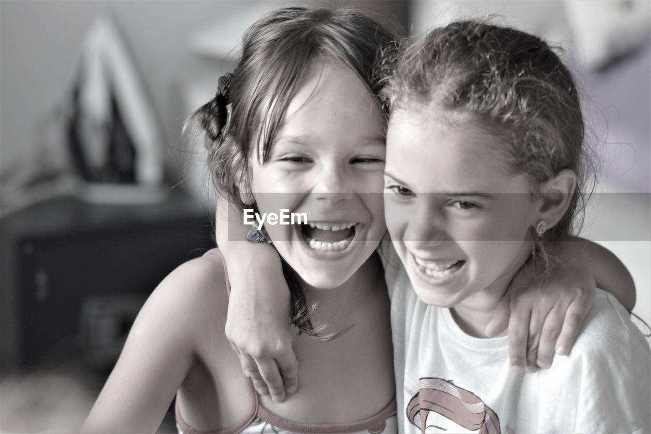 Close-up of happy sisters with arms around standing at home