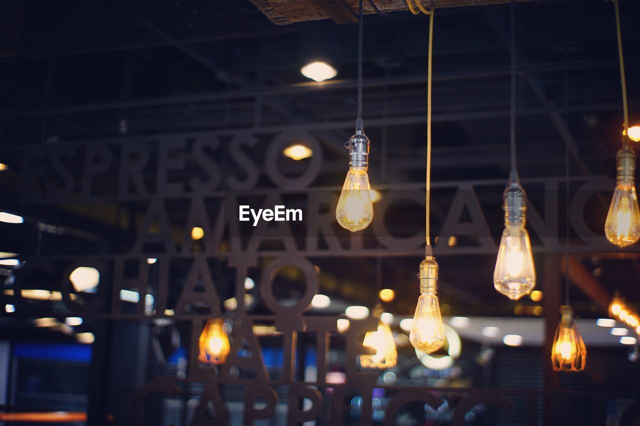 LOW ANGLE VIEW OF ILLUMINATED LIGHT BULB HANGING AT NIGHT