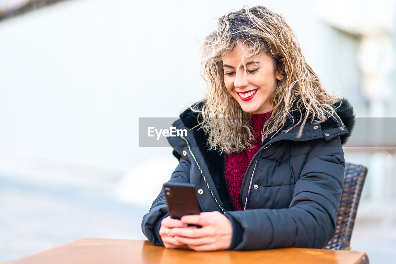 Smiling young woman using mobile phone at table