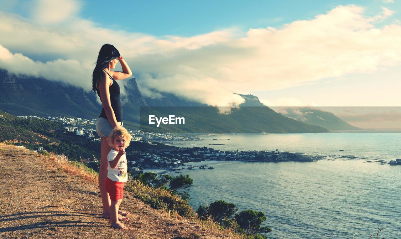 Full length of mother with daughter on hill looking at sea