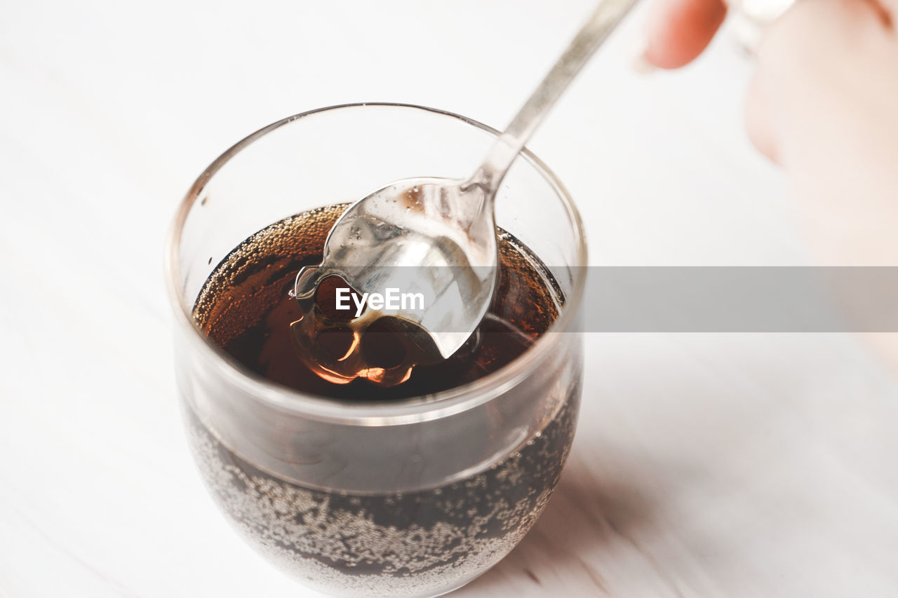 close-up of hand holding drink in glass against white background