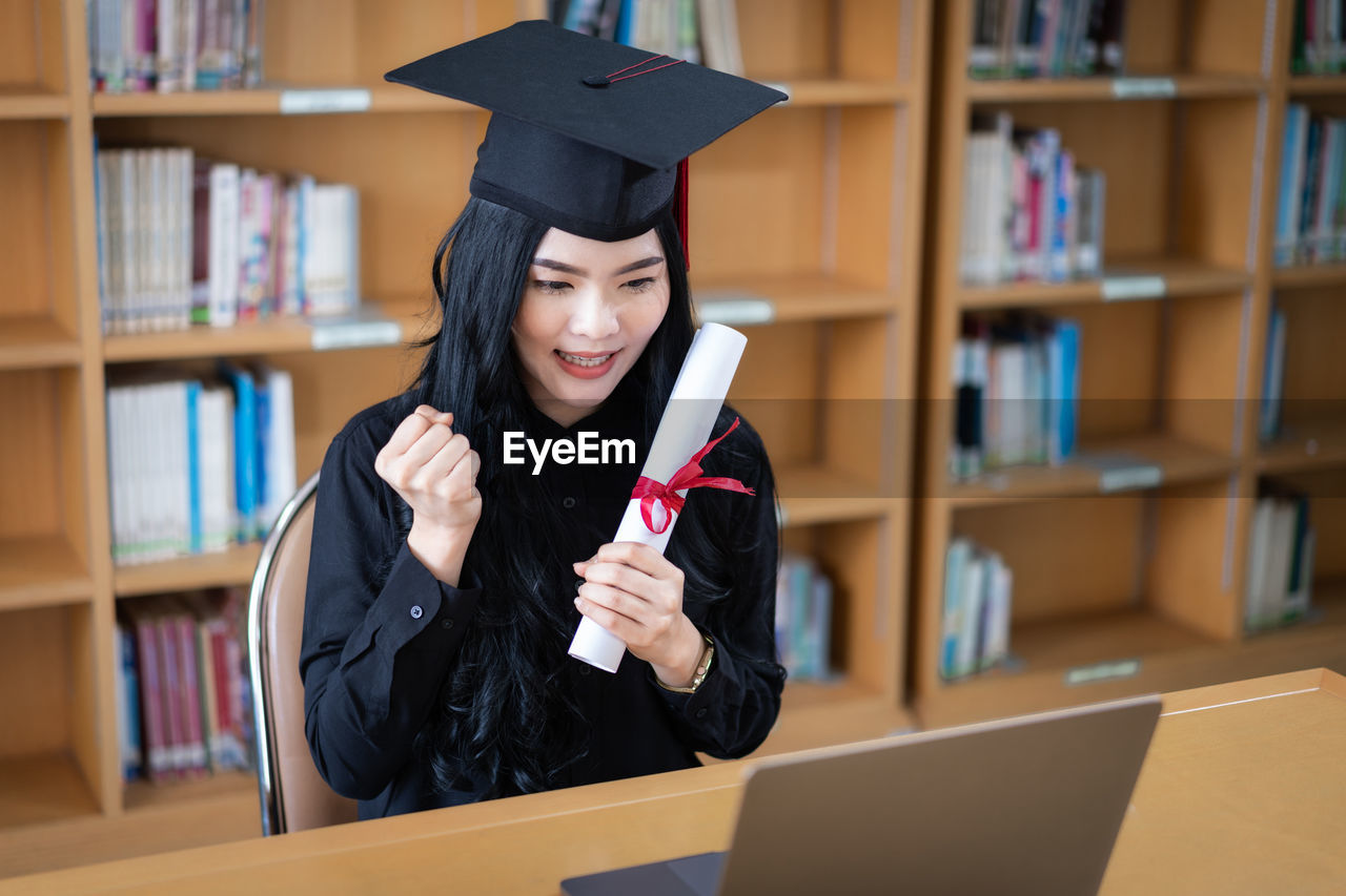 Young woman holding diploma at library