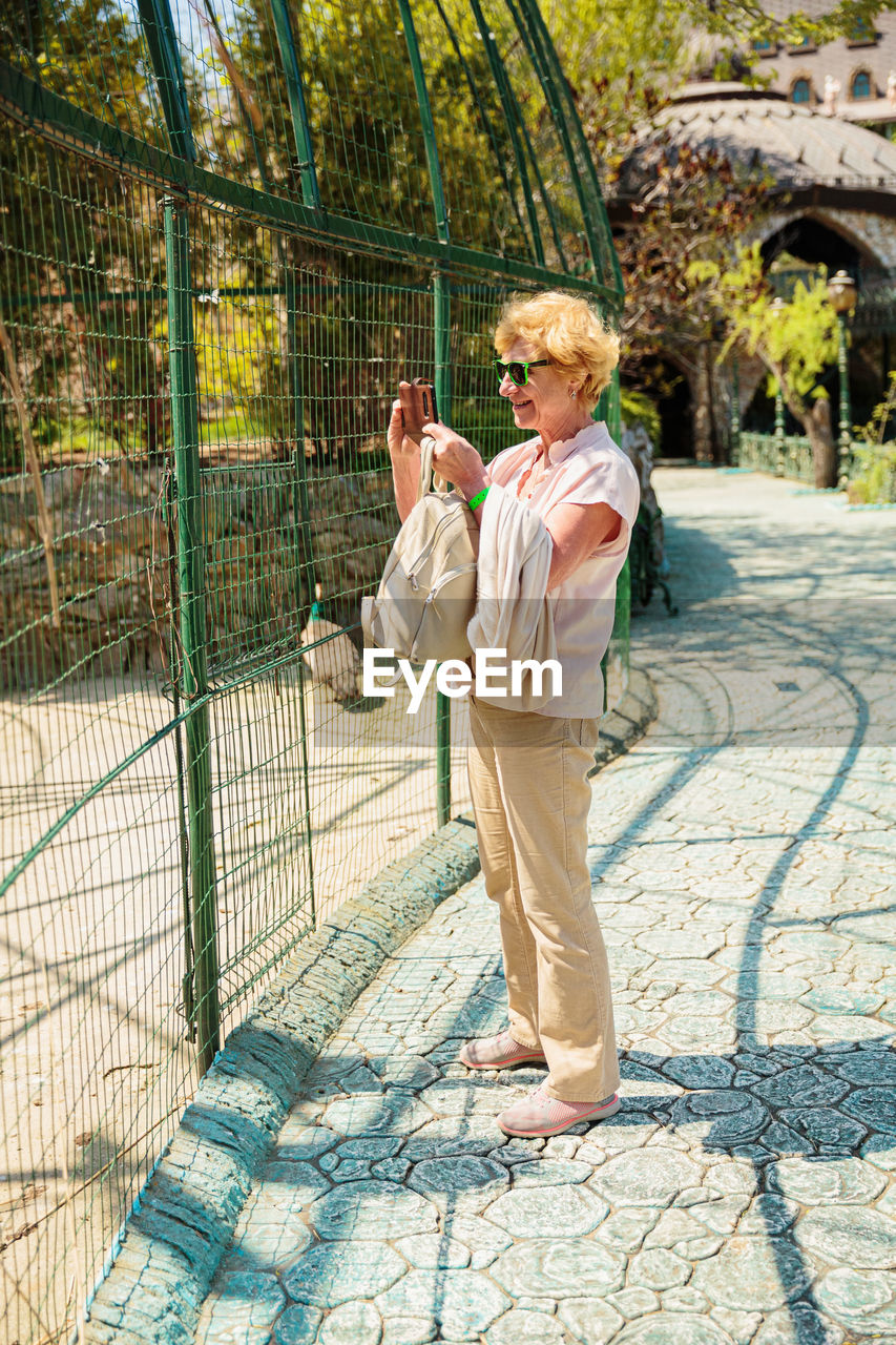 Elderly woman with mobile smartphone taking photo in zoo